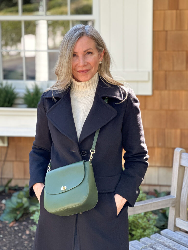 Woman wearing jeans, black coat and green cross body bag.