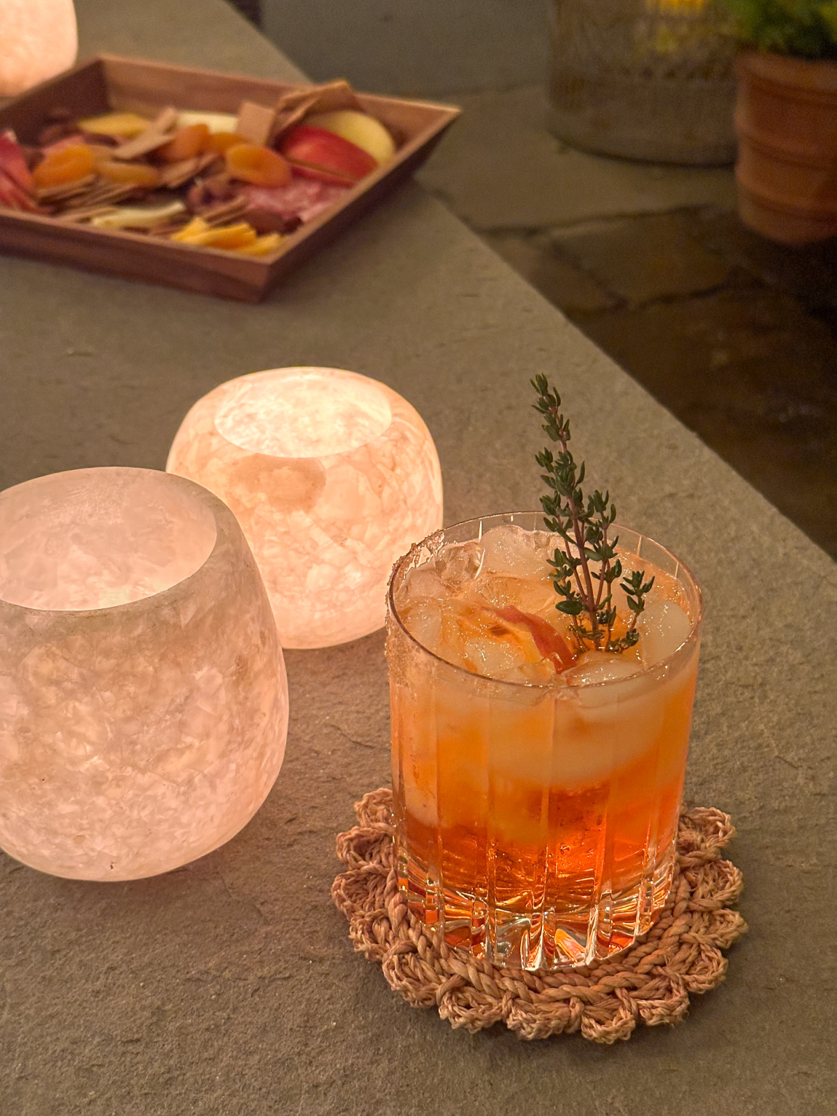 Cocktail, candles and cheese board on outdoor fire table.