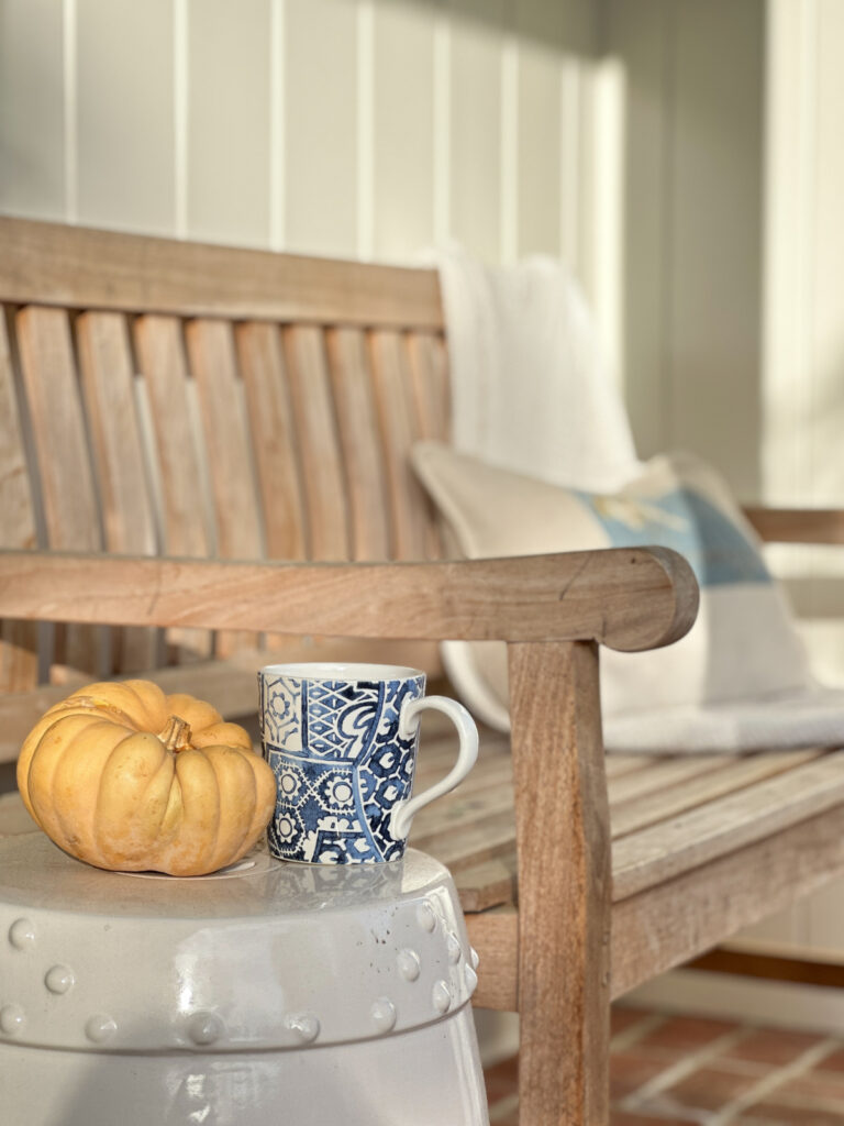 Mug of cocoa next to pumpkin on front porch.