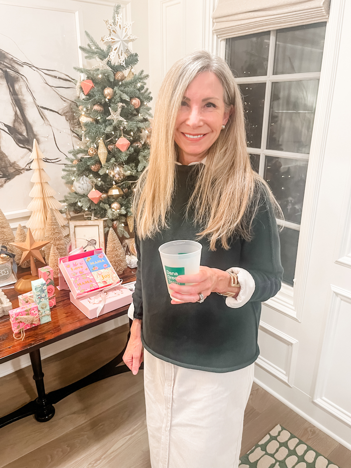 Woman holding cut of wine in front of Christmas display table.