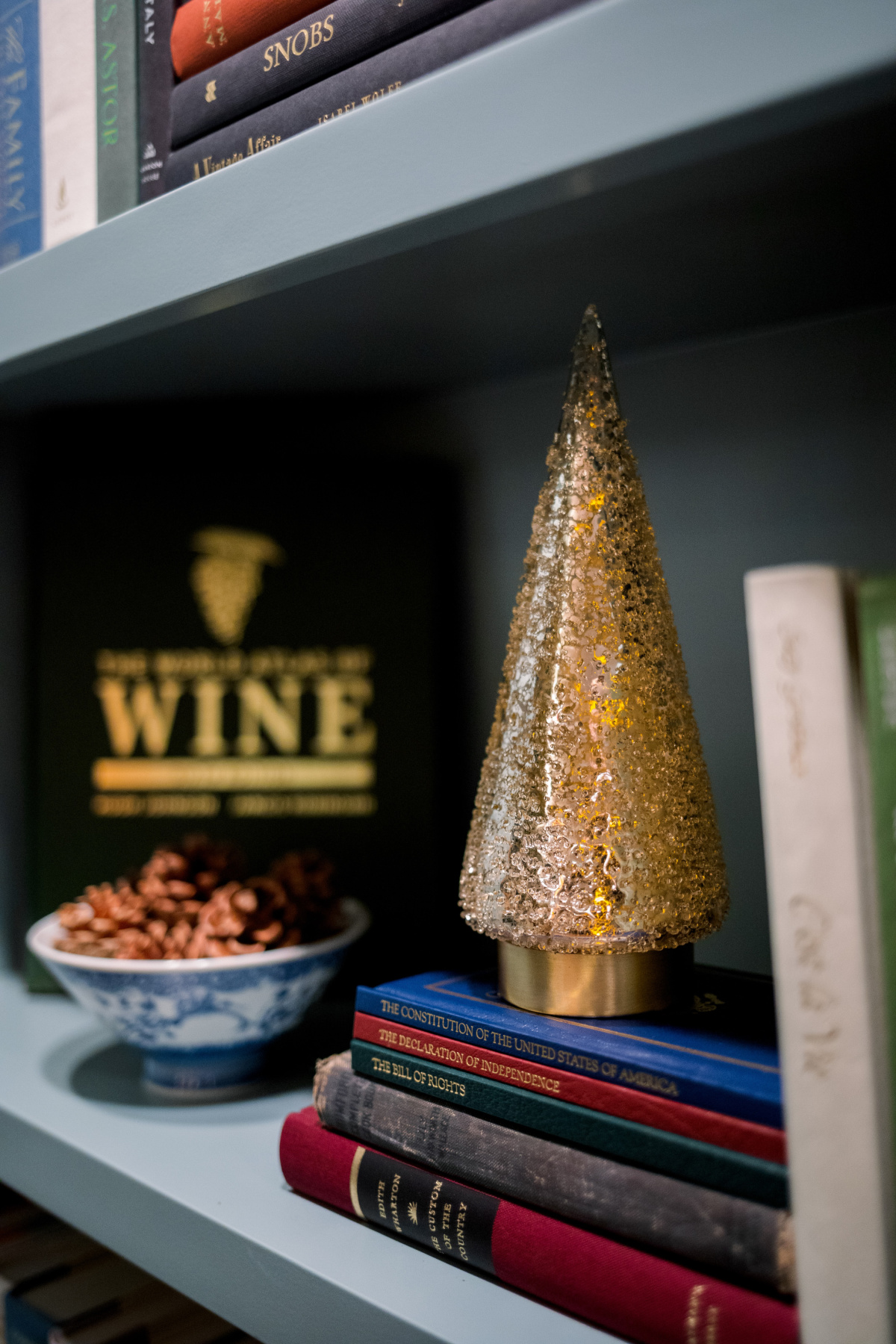 Frosted glass holiday tree and bowl of pinecones on home library shelf. 