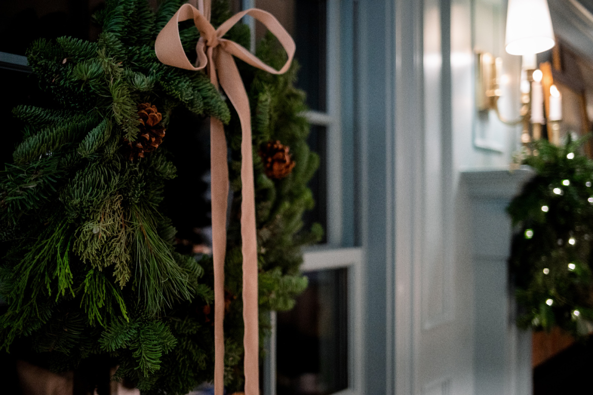 Pine wreath with gold velvet bow hanging in window.
