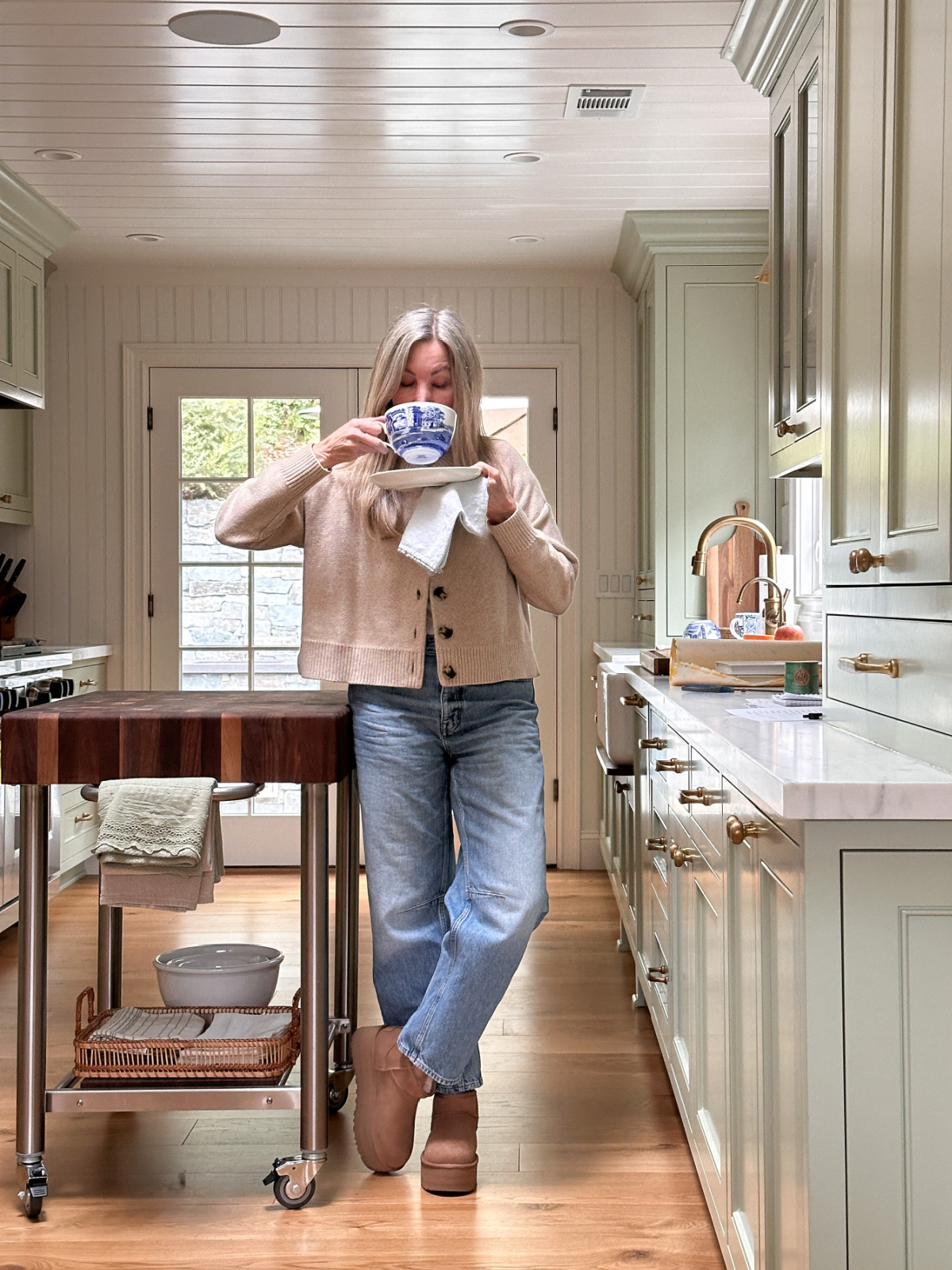 Woman shipping cuppa comfort in green kitchen.