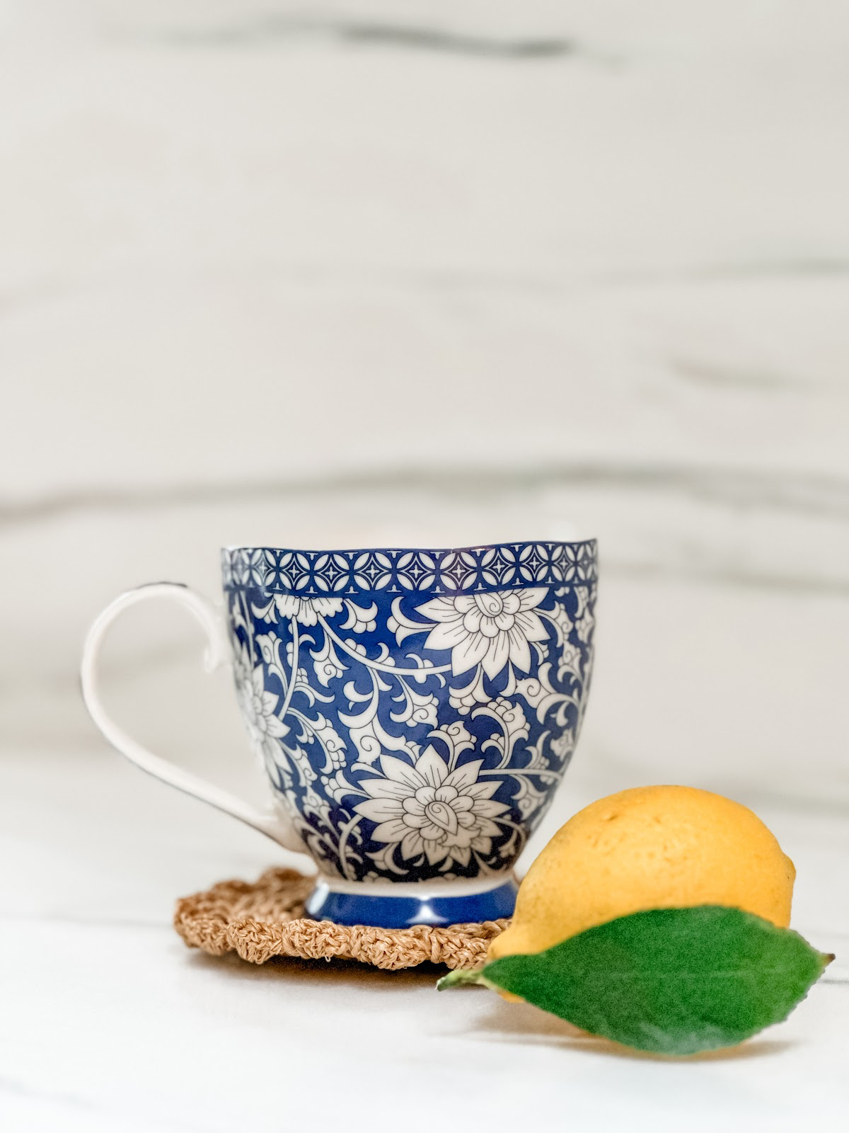 Blue and white mug on woven coaster next to just picked lemon.