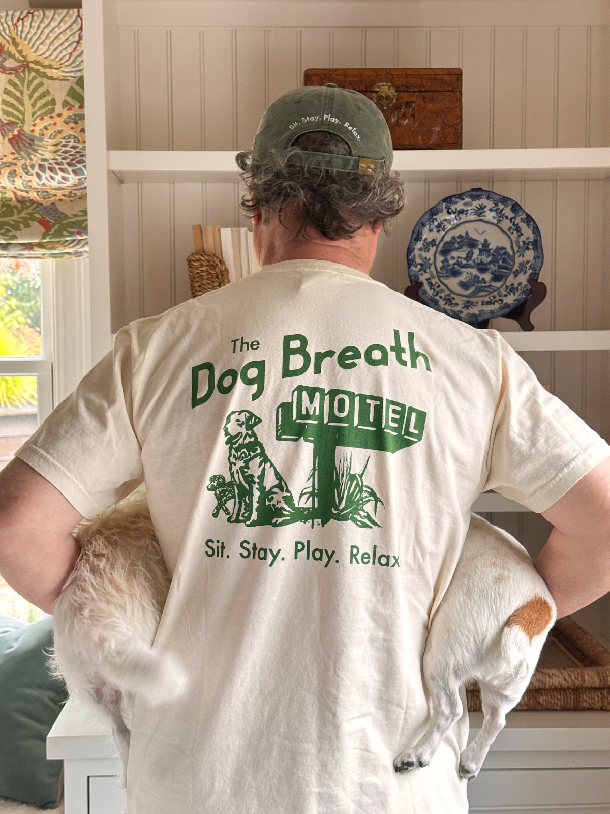 Man holding two small dogs wearing Dog Bread Motel shirt and hat.