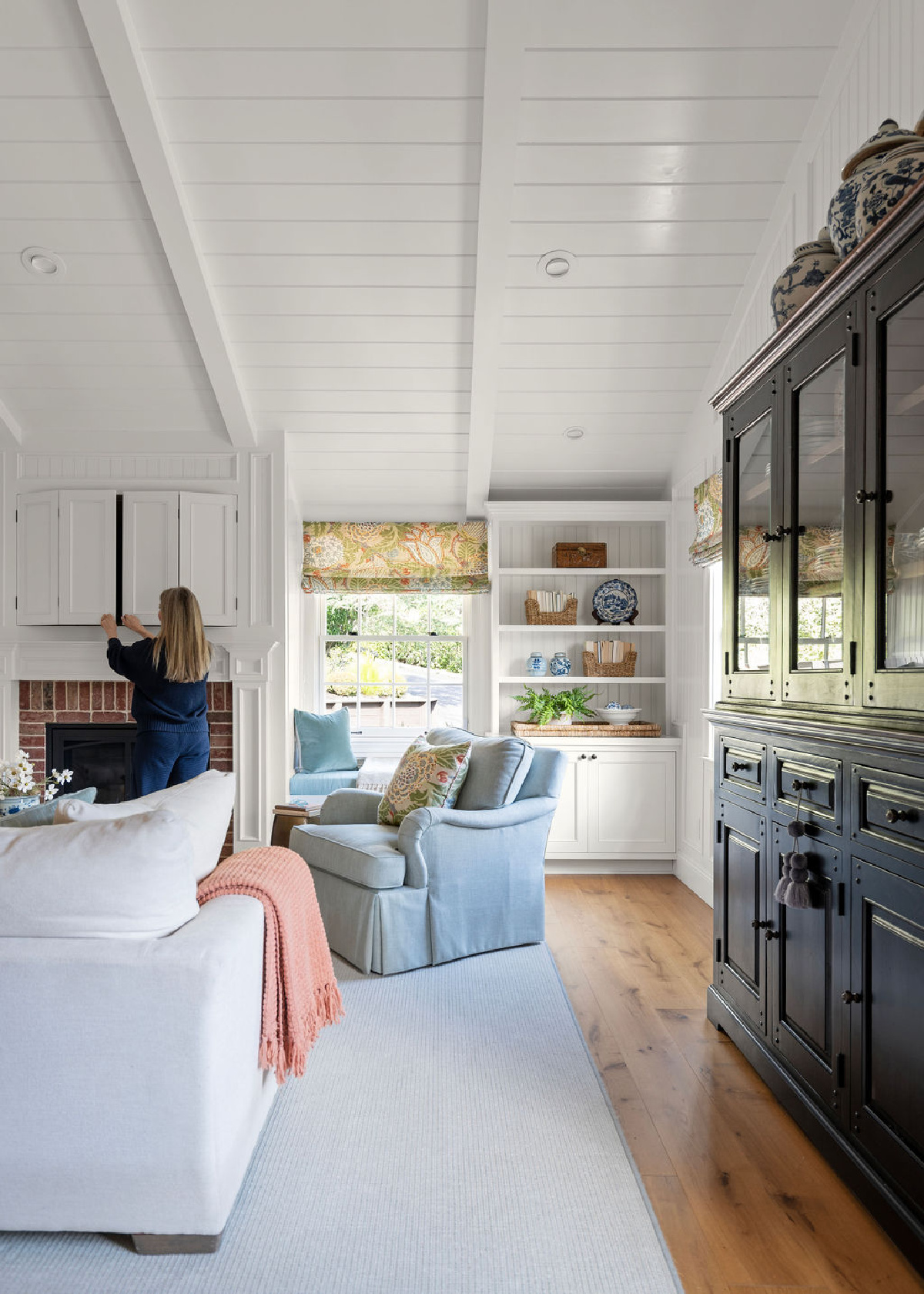 Woman opening recessed TV cabinet in large white great room.