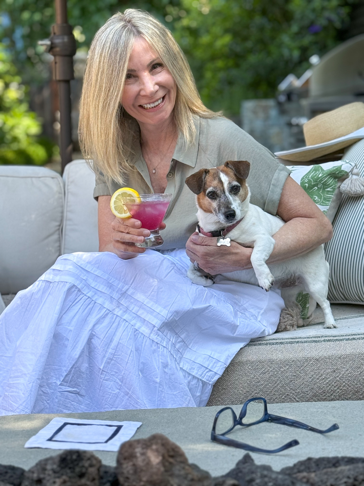 Woman holding Jack Russell Terrier and cocktail on patio.