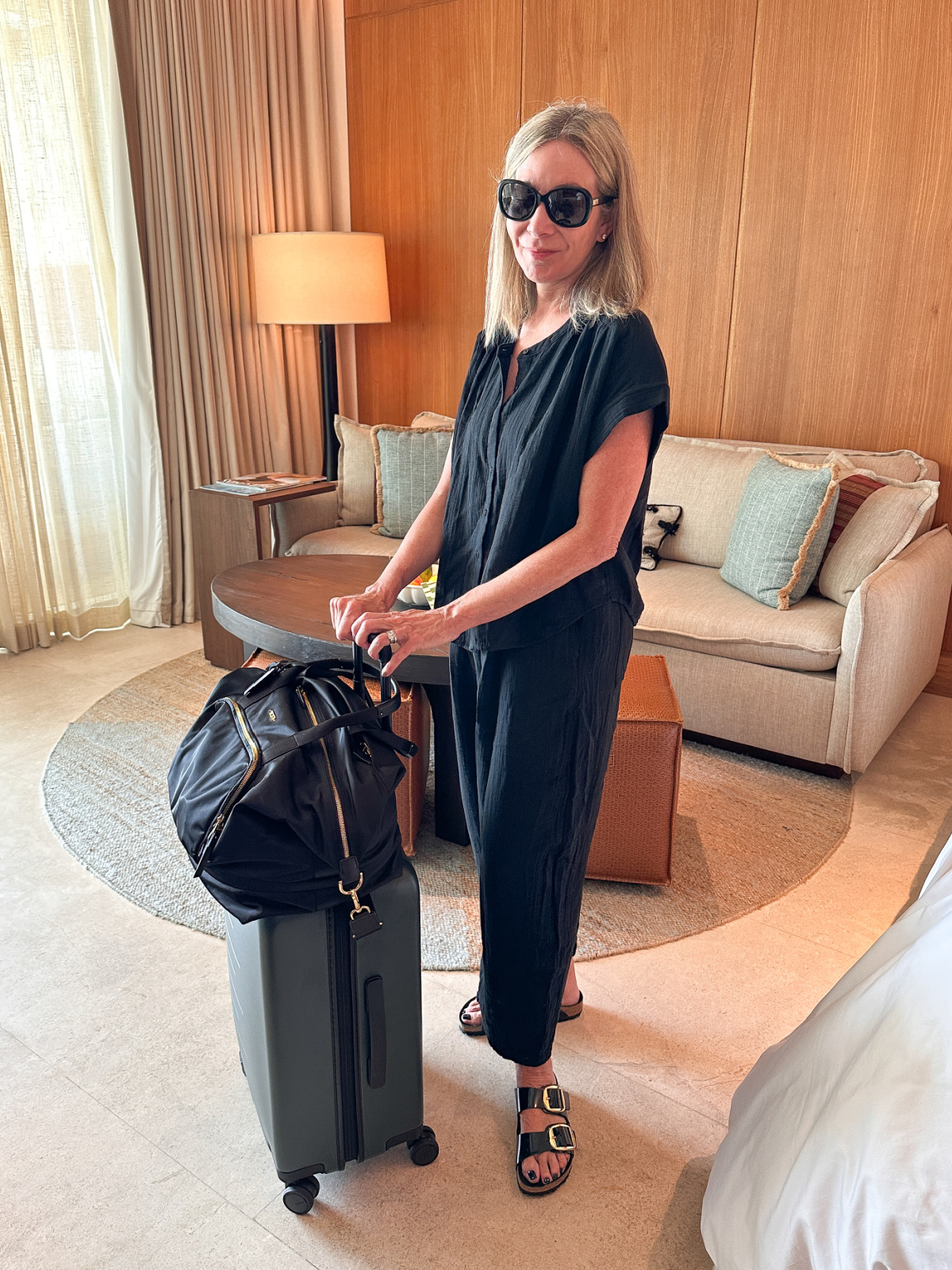Woman wearing Gap gauze set in hotel room with Quince and Tumi luggage.
