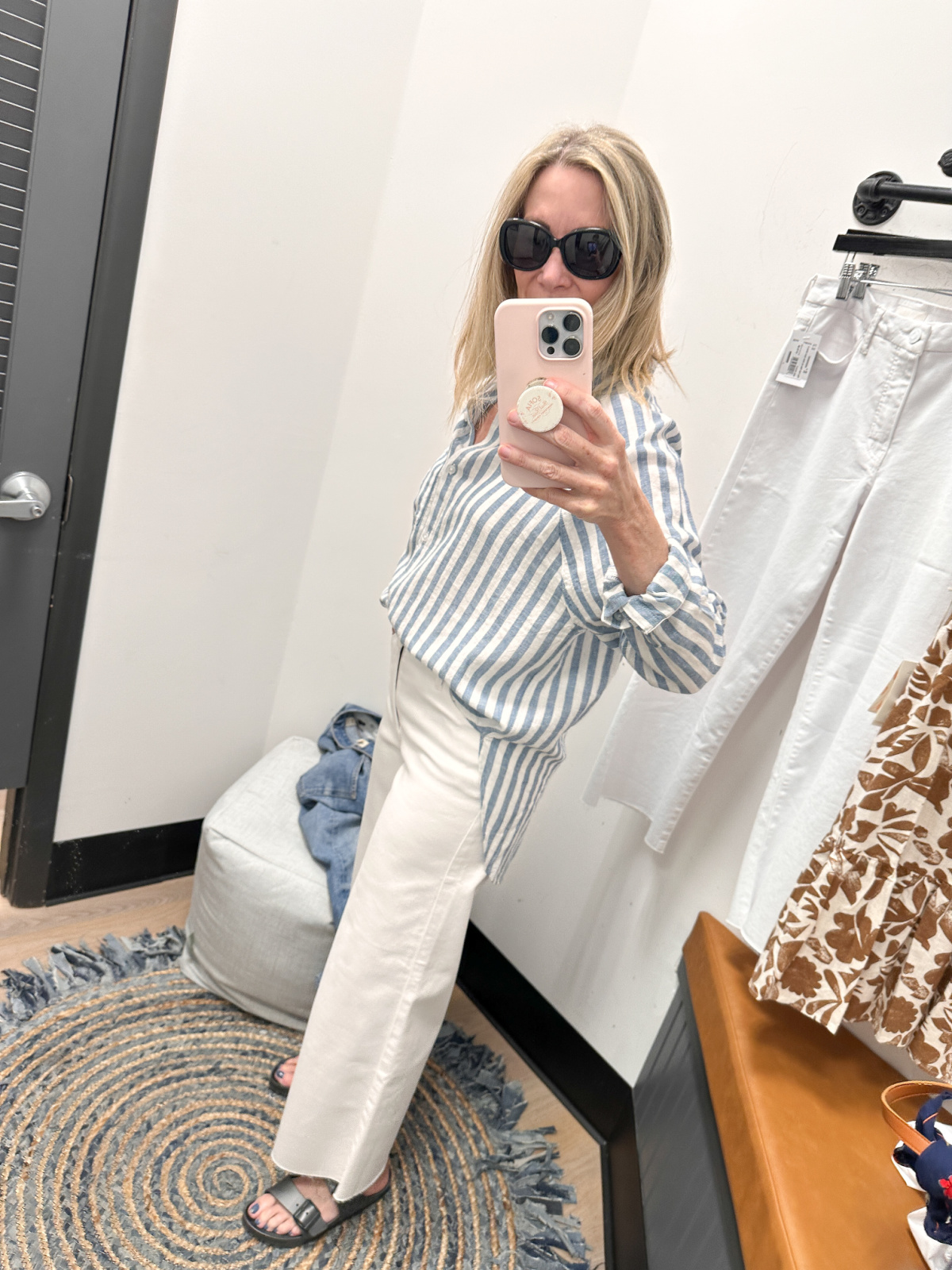 Woman taking dressing room selfie wearing white jeans and striped shirt.
