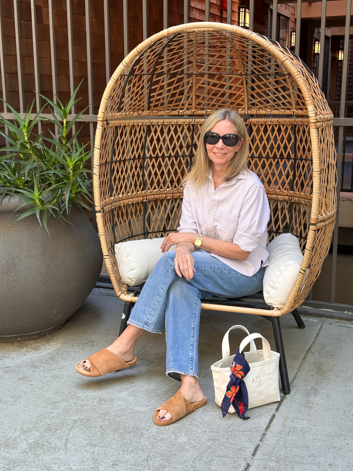 Woman seated in outdoor chair wearing a cropped shirt and jeans.
