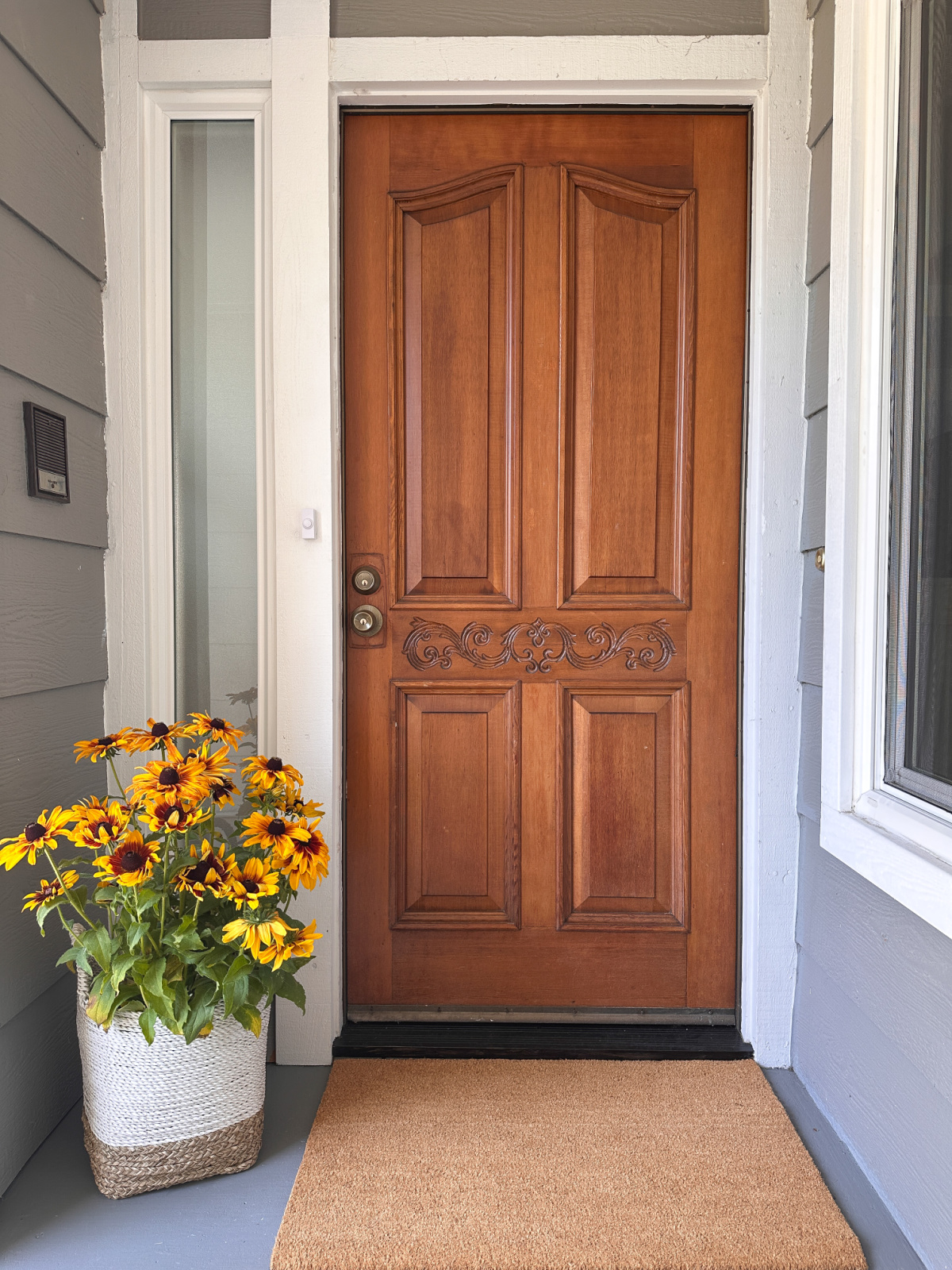 Front door with fall doormat and basket of sunflowers.