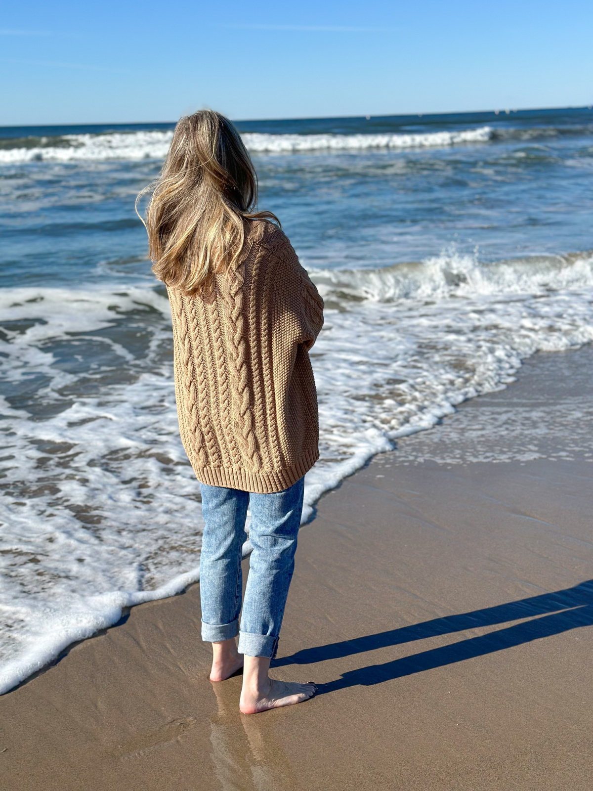Woman on beach wearing Quince cable knit cardigan.