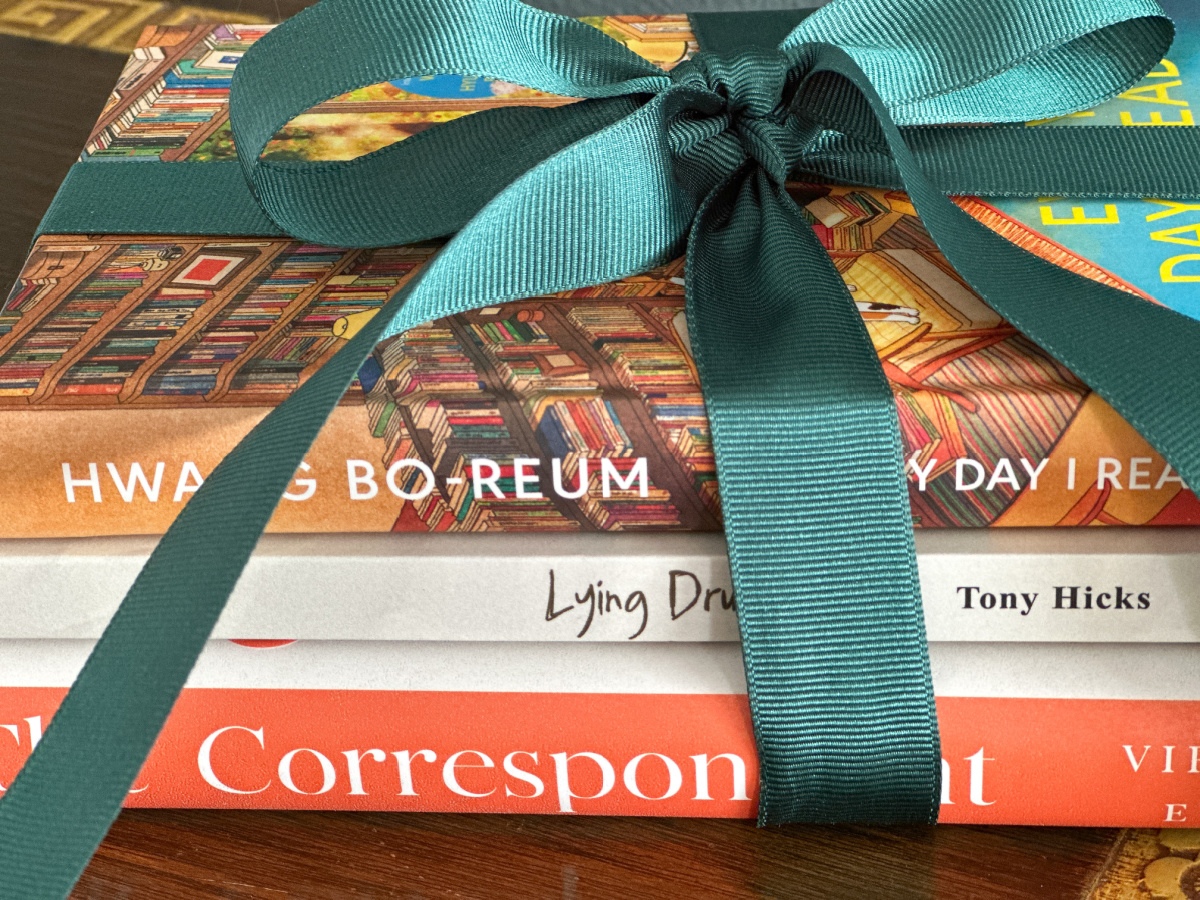 The Correspondent, Lying Drunk, Every Day I Real books bundled together and tied with green ribbon.